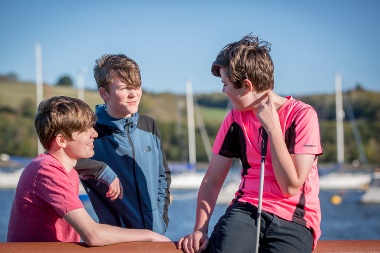 Three male children sit and laugh, one is holding a cane